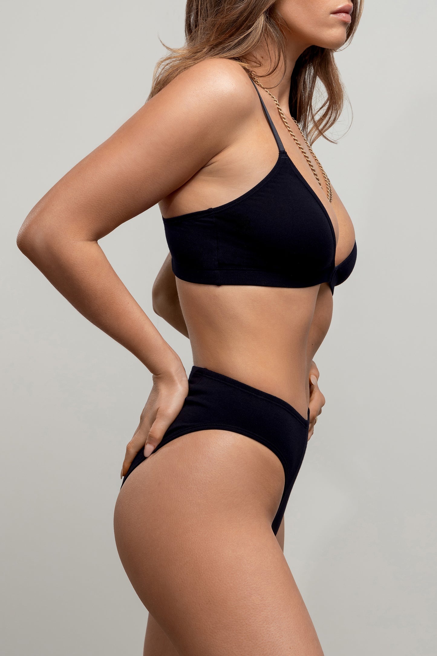 A side view of a model wearing black bralette and knickers